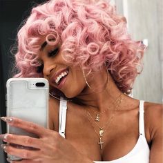 a woman with pink hair is looking at her cell phone while wearing a white tank top