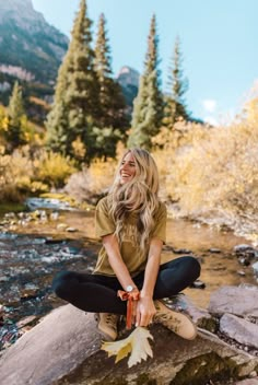 a woman sitting on top of a rock next to a river