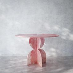 a pink marble table sitting on top of a white floor next to a gray wall