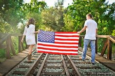 a man and woman holding an american flag on railroad tracks with trees in the background