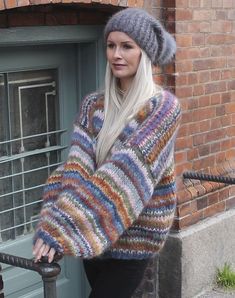 a woman wearing a multicolored sweater and knitted hat is standing on the steps