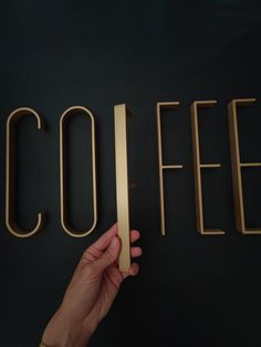 a hand is holding up the word coffee in front of a black background with gold letters