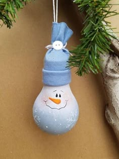 a snowman ornament hanging from a tree branch with a blue hat on it