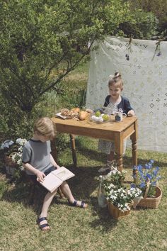 two young children sitting at a table with food and flowers in front of them on the grass