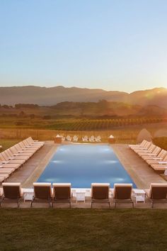 an empty swimming pool with lounge chairs around it and the sun setting in the background