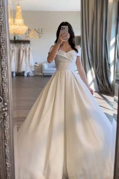 a woman taking a selfie in front of a mirror wearing a white wedding dress