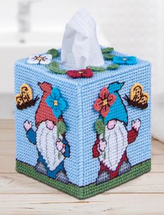 a blue tissue box with gnomes on it sitting on a wooden table next to a toilet paper roll