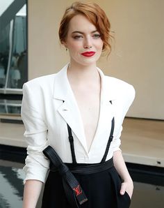 a woman with red hair wearing a white jacket and black pants posing for the camera