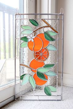 a stained glass window with oranges and leaves on it in front of a window sill