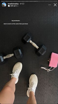 a person standing next to two black dumbs and a pink pad on the floor