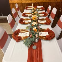 the table is set with orange and white linens, silverware, and flowers