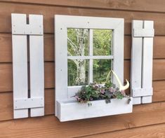 a window with white shutters and flowers in the window sill on a wooden wall