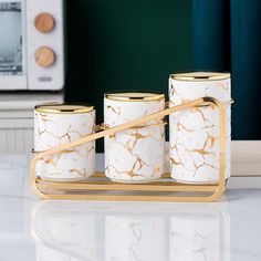 four white and gold canisters sitting on top of a counter next to a toaster oven