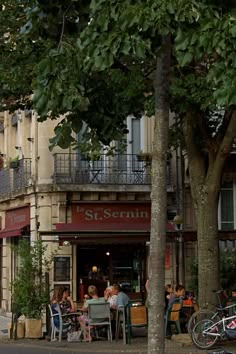 people are sitting at tables in front of a restaurant on the street corner with bicycles parked nearby