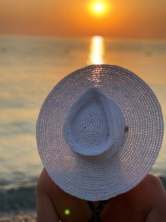 a woman wearing a white hat sitting on top of a beach next to the ocean