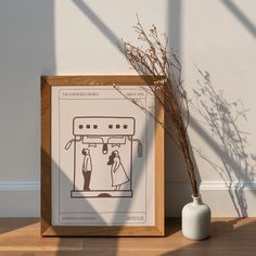 a white vase sitting on top of a wooden table next to a framed poster with a drawing of a man and woman