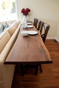 a wooden table with plates and bowls on it in front of a couch next to a window