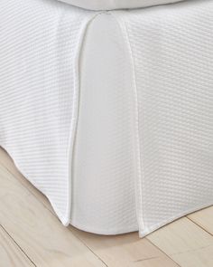 a close up view of a white bed with pleated bedspread