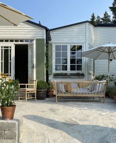 an outdoor patio with chairs, umbrellas and potted plants in front of the house