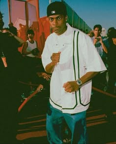 a man standing in front of a crowd wearing a baseball cap and white shirt with green trim