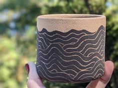 a hand holding up a cup that has wavy designs on the outside, and inside