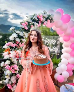 a woman in an orange dress is holding a cake and posing for the camera with balloons around her