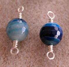 two blue glass beads with silver wire hangers on a carpeted surface in front of a white background