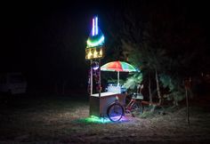 a bike parked under an umbrella in the grass near a light up kiosk