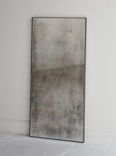 a large mirror sitting on top of a floor next to a white wall with a black frame