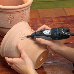 a person using a power tool to cut clay on a wooden table next to potted planters