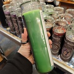 a person holding up a green drink in front of many jars on the shelf at a store