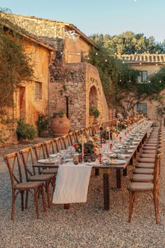 an outdoor dining table set up with chairs and place settings in front of a stone building