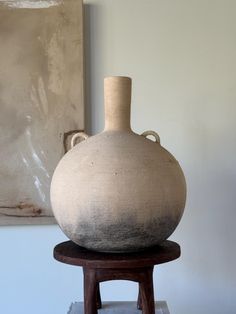 a large white vase sitting on top of a wooden stool in front of a painting