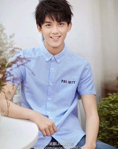 a young man sitting on top of a white chair next to a plant in a pot