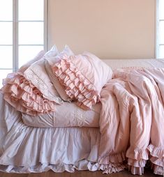 a bed covered in pink ruffled sheets and pillows