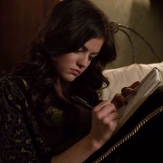 a woman sitting on a couch holding a pen and looking at a book in her hand