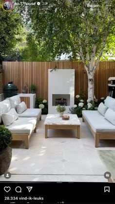 an outdoor living room with white furniture and trees in the back yard, including a fireplace