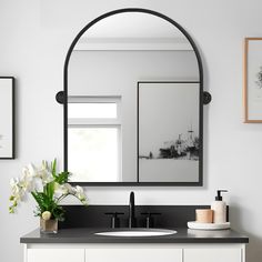 a bathroom with a sink, mirror and flowers on the counter top in front of it