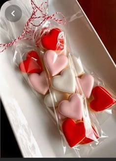 some heart shaped cookies in a plastic bag on a white plate with red twine