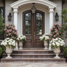 two large white vases filled with pink and white flowers sit on the front steps of a house