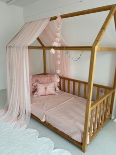 a wooden bed with pink sheets and curtains on it's headboard, in a white room