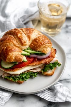 a croissant sandwich with meat, cheese and veggies on it sitting on a white plate