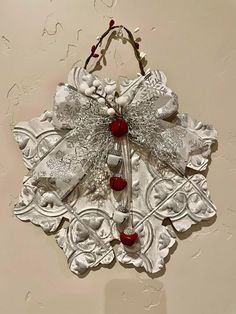 a metal decoration hanging on the wall with red beads and bows attached to it's sides