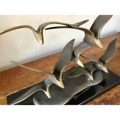 a metal sculpture on a wooden table with birds flying over it's head and wings