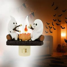 three white ghost figurines sitting on top of a pumpkin in front of bats