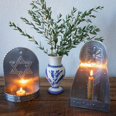 two vases with candles in them on a table next to a plant and candle holder