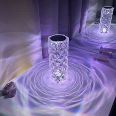 two crystal vases sitting on top of a table next to rocks and purple lights