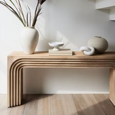 two white vases sitting on top of a wooden table next to a book shelf