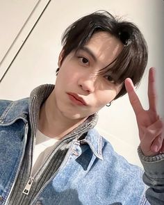 a young man making the peace sign with his hand while wearing a denim jacket and jeans shirt