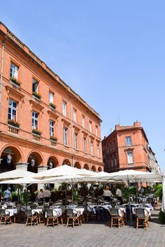 an outdoor restaurant with tables and umbrellas in front of a large red brick building